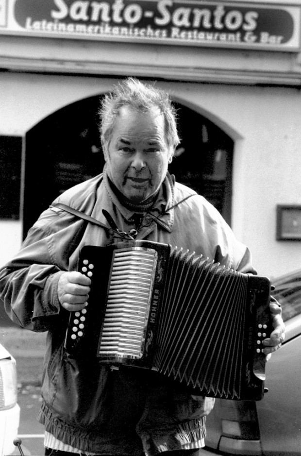A black-and-white portrait depicting Bruno Schleinstein while he plays the accordion in the streets of Berlin. Ekkehard Wölk, 2004. 